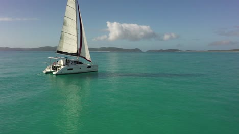 Aerial-orbits-Whitsunday-Yacht-Rental-catamaran-sailboat,-morning-sun