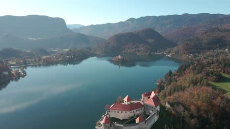 Lowering-aerial-lake-bled-revealing-clifftop-castle-sunny-autumn-day