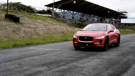 Jaguar-I-Pace,-Elektrisches-Orangefarbenes-Auto,-Vorder--Und-Seitenansicht,-Gefahren-Auf-Der-Rennstrecke