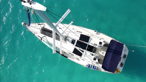 Vogelperspektive-Eines-Segelboots,-Das-Im-Türkisfarbenen-Tropischen-Meer-Vor-Anker-Liegt,-Drohnenaufnahme-Von-Mast-Und-Deck-Von-Oben-Nach-Unten