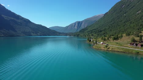 Loads-of-tourists-standing-along-shoreline-of-beautiful-lake-Oldevatn-in-Nordfjord-Norway---Forward-moving-aerial-during-summer-vacation---People-paddling-and-kayaking-in-emerald-green-glacial-lake