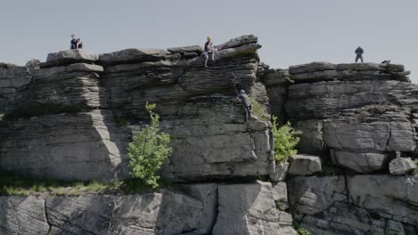 Kletterer-Sitzt-Auf-Einer-Klippe-Und-Blickt-Auf-Seinen-Freund-Herab,-Der-Am-Bamford-Edge-In-England,-Großbritannien,-Klettert