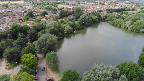 Aerial-view-of-Needham-market-with-alderson-pond-lake-and-the-cityscape-sourrounded-by-green-park-Meadows-vegetation-Classic-English-landscape