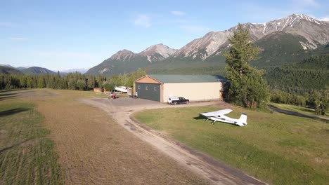 Slowly-flying-over-a-Cessna-206-next-to-a-hanger-over-a-private-grass-runway