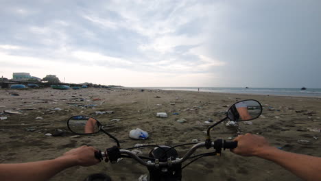 Frontal-tracking-pov-view-of-bike-riding-over-garbage-and-pushing-waste-near-beach-over-massive-garbage-dump-site
