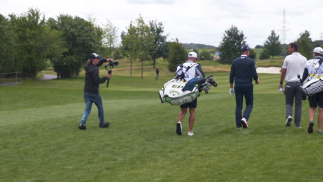 Kameramann-Filmt-Golfspieler-Mit-Ausrüstung,-Die-Auf-Dem-Golfplatz-Laufen