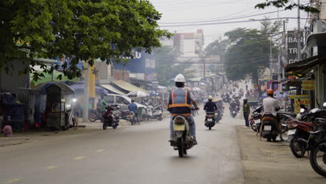 Southeast-Asia-street-scene,-people-riding-moped-scooters-down-paved-road