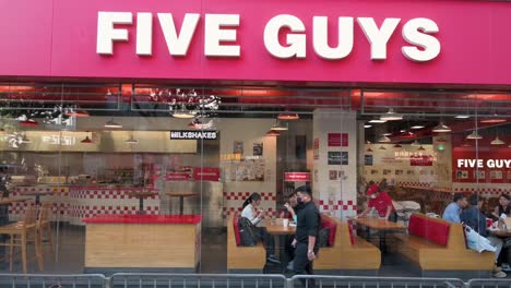 Los-Peatones-Pasan-Junto-A-La-Cadena-Multinacional-Estadounidense-De-Restaurantes-De-Comida-Rápida-Five-Guys-Y-Su-Logotipo-Mientras-Los-Clientes-Comen-Dentro-Del-Establecimiento-En-Hong-Kong.