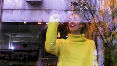 Frau-Trägt-Ein-Gelbes-Hemd,-Während-Sie-Eine-Schneeflocke-Auf-Das-Fenster-Einer-Bar-Zeichnet