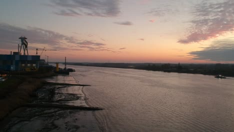 Aerial-view-of-the-river-Schelde-with-a-boat-sailing-into-a-colorful-sunset