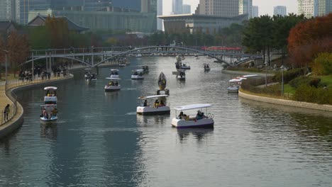 Menschen,-Die-Bei-Sonnenuntergang-Wasserattraktionen-Im-Songdo-Central-Park-In-Incheon-Machen-–-Bootfahren-Und-Reisen-Mit-Mondbooten-Auf-Einem-See