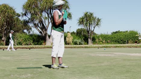 An-elderly-woman-in-club-colors-delivers-a-wood-during-a-lawn-bowls-competition