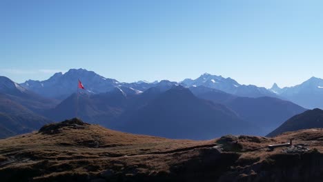 Wunderschöne-Luftaufnahme-Im-Bergpanorama-Mit-Matterhorn,-Schweizer-Flagge-Und-Einem-Wanderer