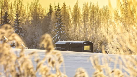 Remote-tiny-cabin-house-in-snow-landscape-with-golden-hour-sunlight,-timelapse