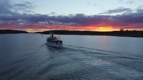 Static-aerial-view-of-MS-Rudolfina-sailing-out-with-a-spectacular-burning-orange-cloudy-sunset-in-the-horizon