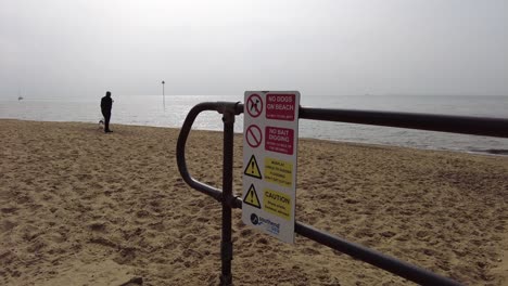 Person-on-beach-walking-dog-with-No-dog-sign-English-beach
