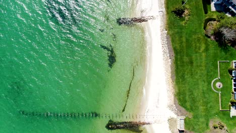 Remains-of-old-pier-and-crystal-clear-ocean-water-near-sandy-coastline,-aerial-view