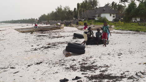 Niños-Africanos-Haciendo-Volteretas-De-Neumáticos-Apilados-En-La-Playa,-Zanzíbar