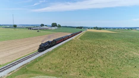An-Aerial-Ride-Along-View-of-a-Steam-Engine-Puffing-Smoke-and-Steam-with-Passenger-Coaches-Traveling-on-a-Single-Track-Fertile-Farmland-and-Countryside-With-a-Farmer-Working-in-the-Background