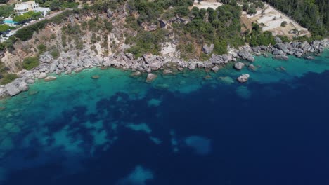 Aerial-rocky-sea-shore-with-clear-blue-water-at-Lefkada,-Greece:-drone-flying-shot