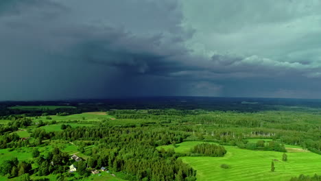 Aerial-shot-from-left-to-right-of-rainfall-in-the-background-over-scenic-farmland-with-trees-in-the-countryside
