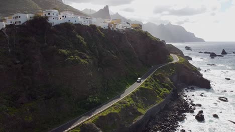 Aerial-drone-view-of-a-coastal-road-and-a-village-above-it-in-Benjio,-Anaga-National-Park,-Northern-Tenerife,-the-Canary-Islands