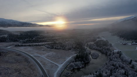 Flying-over-foggy-icy-treetops-and-frozen-fields-at-sunset-in-Northern-Scandinavia-Helgeland,-Northern-Norway