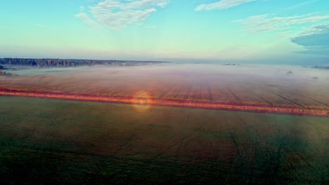 Aerial-view-of-mystic-fog-hovering-over-harvested-wheat-field-in-rural-countryside-during-sunny-day-with-blue-sky-in-the-morning