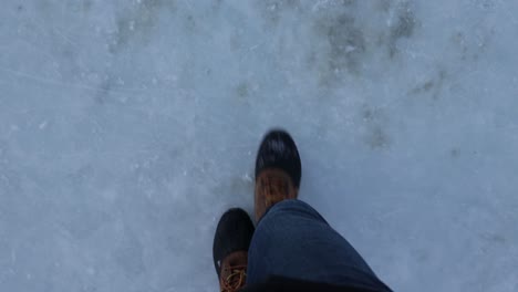 Topdown-point-of-view-Snow-boots-walking-on-Frozen-lake-surface,-Slow-motion