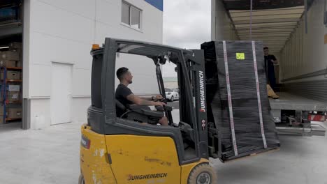 Forklift-loading-solar-panel-crate-in-a-shipping-truck-by-two-employees-at-Allo-Solar,-Pan-right-follow-shot