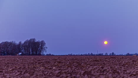Time-lapse-shot-of-sinking-full-moon-at-blue-sky-over-agricultural-farm-field-at-night