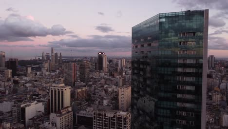 Drone-shot-over-downtown-of-Buenos-Aires-with-modern-glass-building-in-foreground-during-purple-sunset-at-horizon---Argentina,South-America