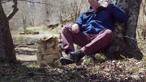 Senior-man-with-blue-jacket-sits-in-wood-to-rest-and-drink-water