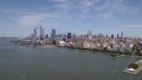 Aerial-view-of-a-helicopter-flying-over-the-Hudson-river-in-front-of-the-Midtown-Manhattan-cityscape,-sunny,-summer-day-in-NYC,-USA