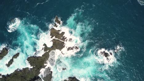 Aerial-top-down-shot-of-coral-rocks-hitting-by-sea-waves-during-sunny-day-in-Yogyakarta,Indonesia