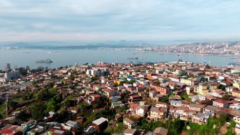 Aerial-dolly-in-of-Playa-Ancha-Hill-neighborhood-houses-near-sea-port,-container-cargo-ships-in-background,-Valparaíso,-Chile