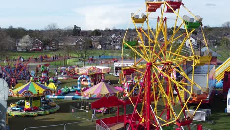 Small-town-fairground-Easter-holidays-funfair-rides-in-public-park-aerial-view-across-Ferris-wheel
