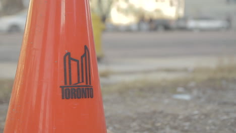 Fokussierter-Orangefarbener-Toronto-Pylon-Mit-Verschwommenen-Autos-Und-Fahrenden-Und-Gehenden-Menschen-Im-Hintergrund-Im-Norden-Von-Ontario,-Toronto,-Kanada