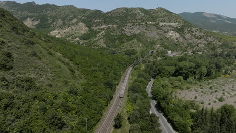 Vista-Aérea-Del-Tren-De-Carga-Que-Viaja-Al-Túnel-Ferroviario-Que-Pasa-Por-La-Montaña-En-Mtskheta,-Georgia