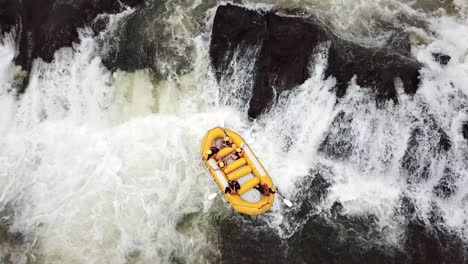 Aerial-drone-top-view-of-a-yellow-rafting-boat-attempting-to-move-down-a-waterfall-on-the-Nile-River-in-Jinja,-Uganda