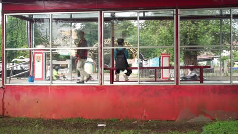 students-sit-in-long-chairs-at-the-bus-transit-stop-and-pass-the-cleaning-service-officer-in-Semarang,-Indonesia-on-June-11,-2022