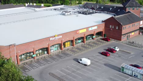 Aerial-view-flying-above-Morrisons-supermarket-car-park-in-rural-Warrington-countryside-village-zoom-out-shot