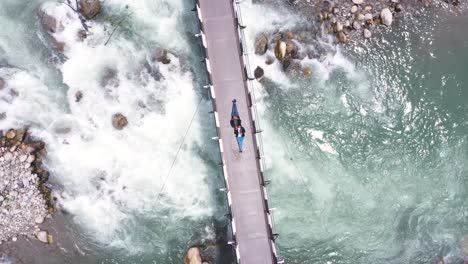 Aerial-drone-bird's-eye-view-over-a-couple-lying-down-over-a-hanging-bridge-over-a-river-while-on-the-way-to-Manali,-Himachal-Pradesh,-India