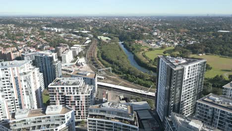 Aerial-Shot-Flying-forward-among-the-Residential-Apartments-in-Sydney-Suburb-with-tall-buildings,-train-lines,-and-park-in-the-Background,-beautiful-summer-day-with-bright-green-trees-and-grass