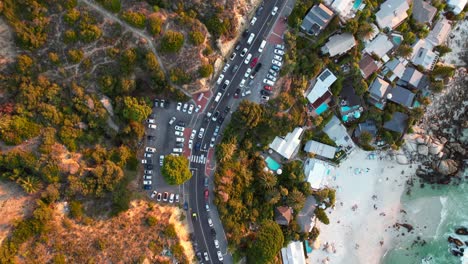 top-down-of-Clifton-beach-road-with-traffic-driving-at-sunset-in-Cape-Town,-aerial
