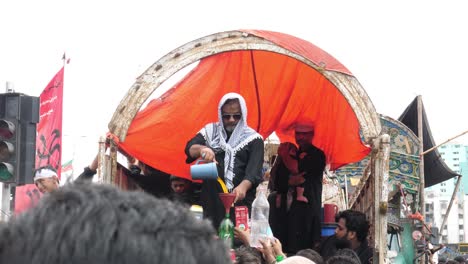 At-the-juloos-or-parade-of-Muharram,-also-known-as-Muharram-Ul-Haram,-a-guy-is-pouring-orange-sharbat-for-the-mourners-to-drink-from-a-decorated-platform-in-Pakistan