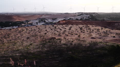 High-angle-shot-of-sand-dunes-with-the-view-of-windmills-rotating-in-the-background-in-Vietnam-at-daytime