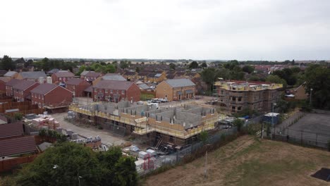 High-to-low-angle-rotating-gimbal-drone-shot-of-a-building-development-site-in-Bedfordshire,-England,-Uk-on-a-neutral,-cloudy-day-from-surrounding-fields