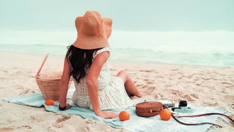 Female-photographer-is-sitting-down-and-putting-her-sunglasses-on-to-relax-at-the-beach-near-the-water-waves