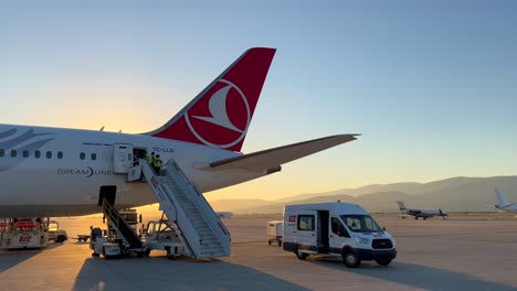 Flugpersonal-Kommt,-Um-Den-Airbus-Der-Türkischen-Fluggesellschaft-Am-Internationalen-Flughafen-Zu-Reinigen,-Gelandetes-Flugzeug-Mit-Wunderschönem-Sonnenuntergang,-Arbeitende-Menschen,-4K-Aufnahme